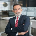 Professional businessman sitting confidently in a modern office with multiple screens displaying data.